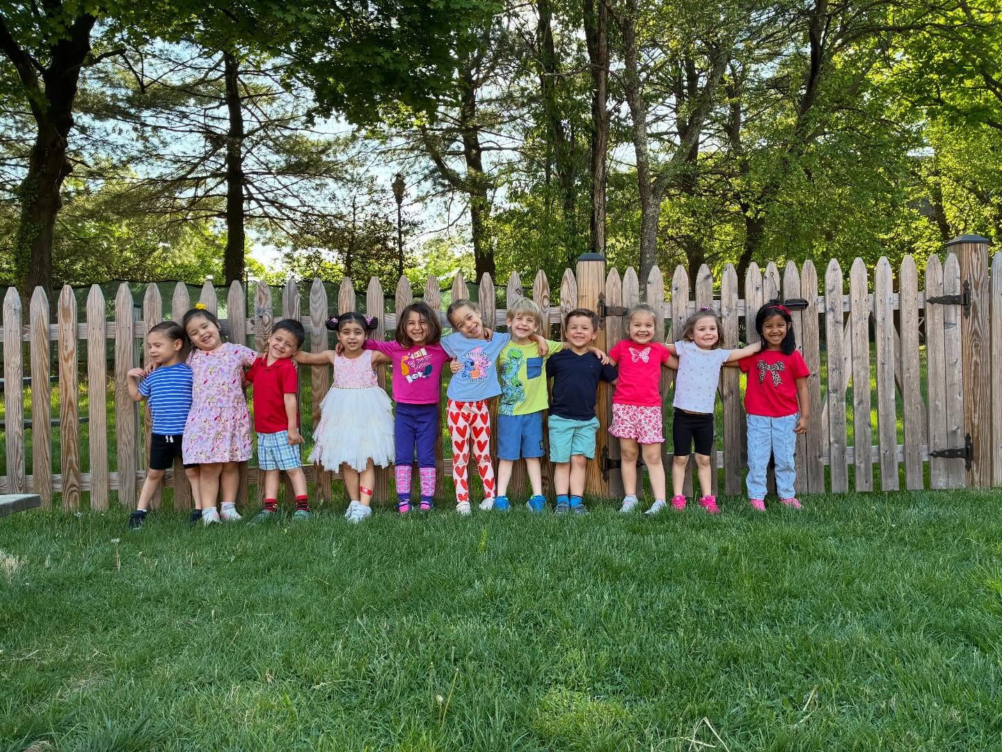 Preschool students lined up and smiling at the playground fence